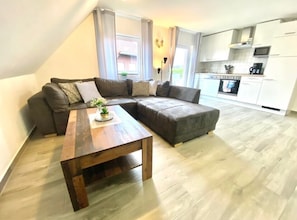 Una sala moderna con una mesa de centro de madera, dos sofás grises y una cocina al fondo.