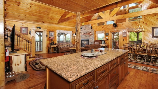 A spacious log cabin interior with a large kitchen island, wooden dining table, and a cozy fireplace. - A Cloud 9 - Mountain Views, Hot Tub Bliss & Pool Table Fun! (Sevierville)