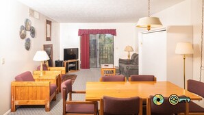 Uma sala de estar acolhedora com uma mesa de jantar de madeira, cadeiras roxas, um sofá e uma televisão.