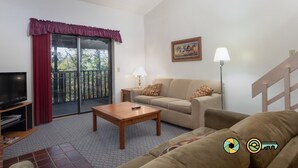 Un salon comprenant un canapé, une table basse, un téléviseur et un balcon avec une porte coulissante.