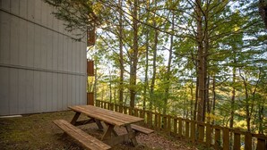 Une table de pique-nique dans un espace boisé, avec une clôture en bois et un bâtiment en arrière-plan.