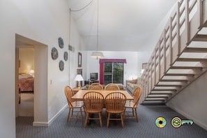A dining area with a wooden table and chairs, a television, and a staircase.