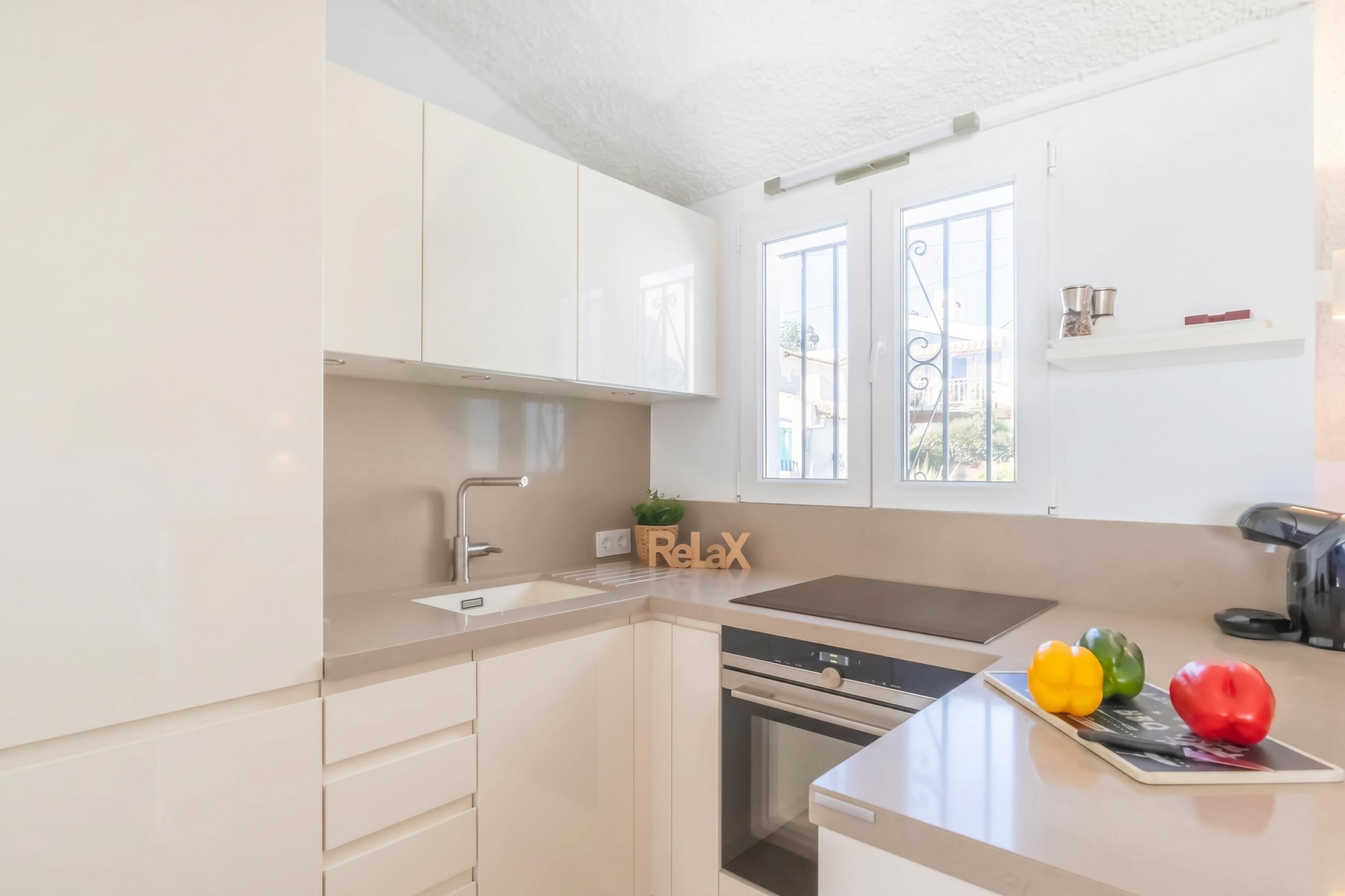 Une cuisine avec des meubles blancs, un évier, une cuisinière et un plan de travail agrémenté d’une plante et d’une pancarte indiquant « Détendez-vous ».