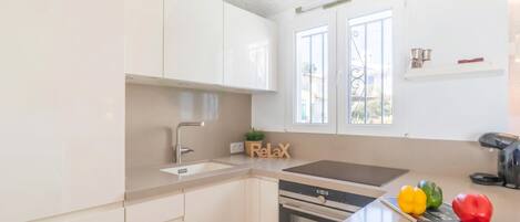 Une cuisine avec des meubles blancs, un évier, une cuisinière et un plan de travail agrémenté d’une plante et d’une pancarte indiquant « Détendez-vous ».