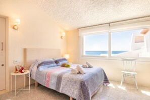 A bedroom with a bed, a small table with a bottle, a chair, and a window with a view.