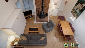 Ein Wohnzimmer mit hohen Decken, einem Kamin, einer Couch, einem Fernseher und einem Essbereich mit Stühlen und einem Tisch.