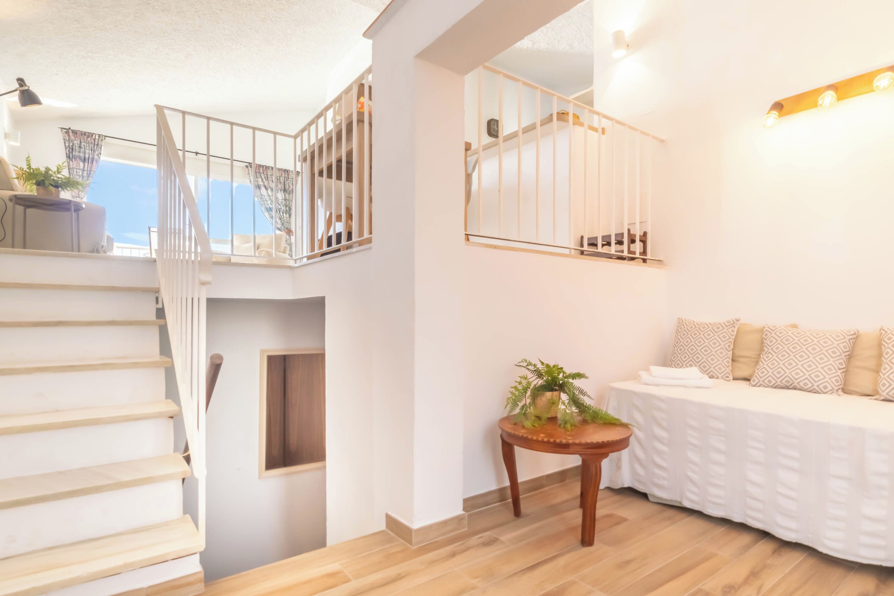 A staircase leading to a balcony with a railing, a sofa with patterned cushions, and a small table with a plant.