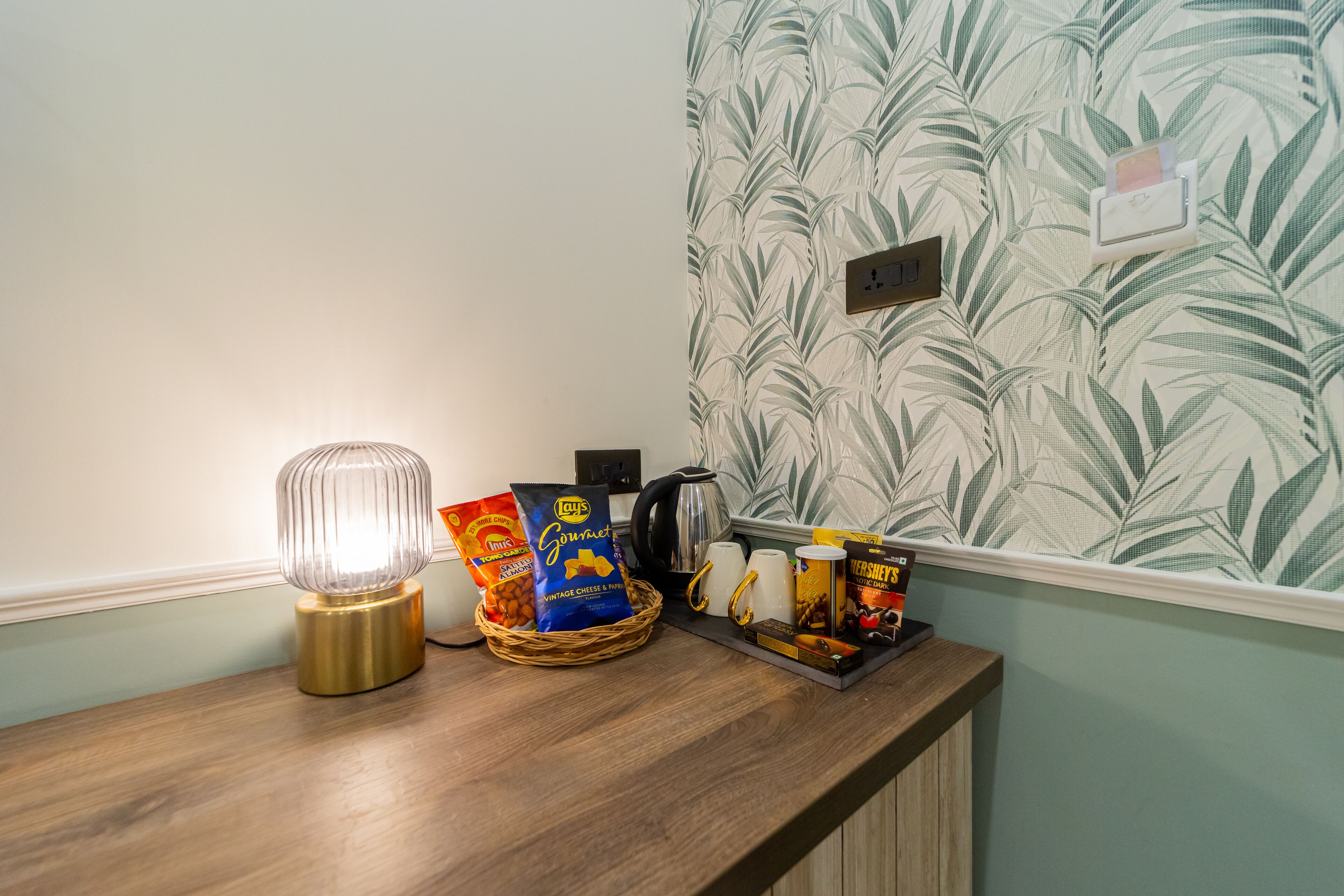 A wooden counter with a lamp, snacks, and a coffee maker.