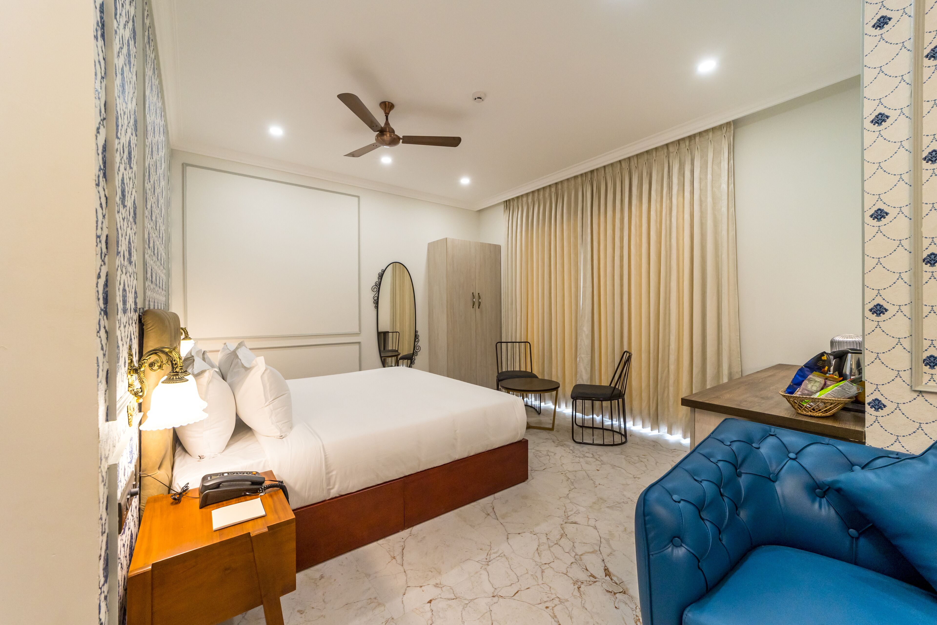 Une chambre d’hôtel avec un lit, une table de chevet, une lampe, un miroir, une armoire et un canapé bleu.