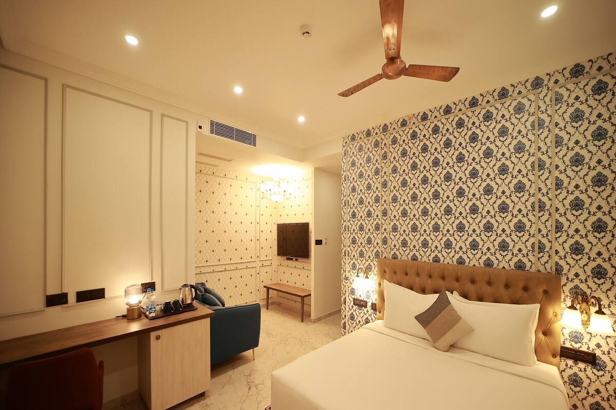 A hotel room with a bed, a desk, a chair, a ceiling fan, and patterned wallpaper.