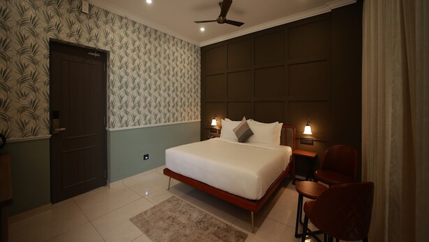 A bedroom with a bed, a desk, a chair, a ceiling fan, and a door. - De Fleur Hotel (Puducherry)