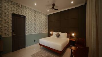 A bedroom with a bed, a desk, a chair, a ceiling fan, and a door.
