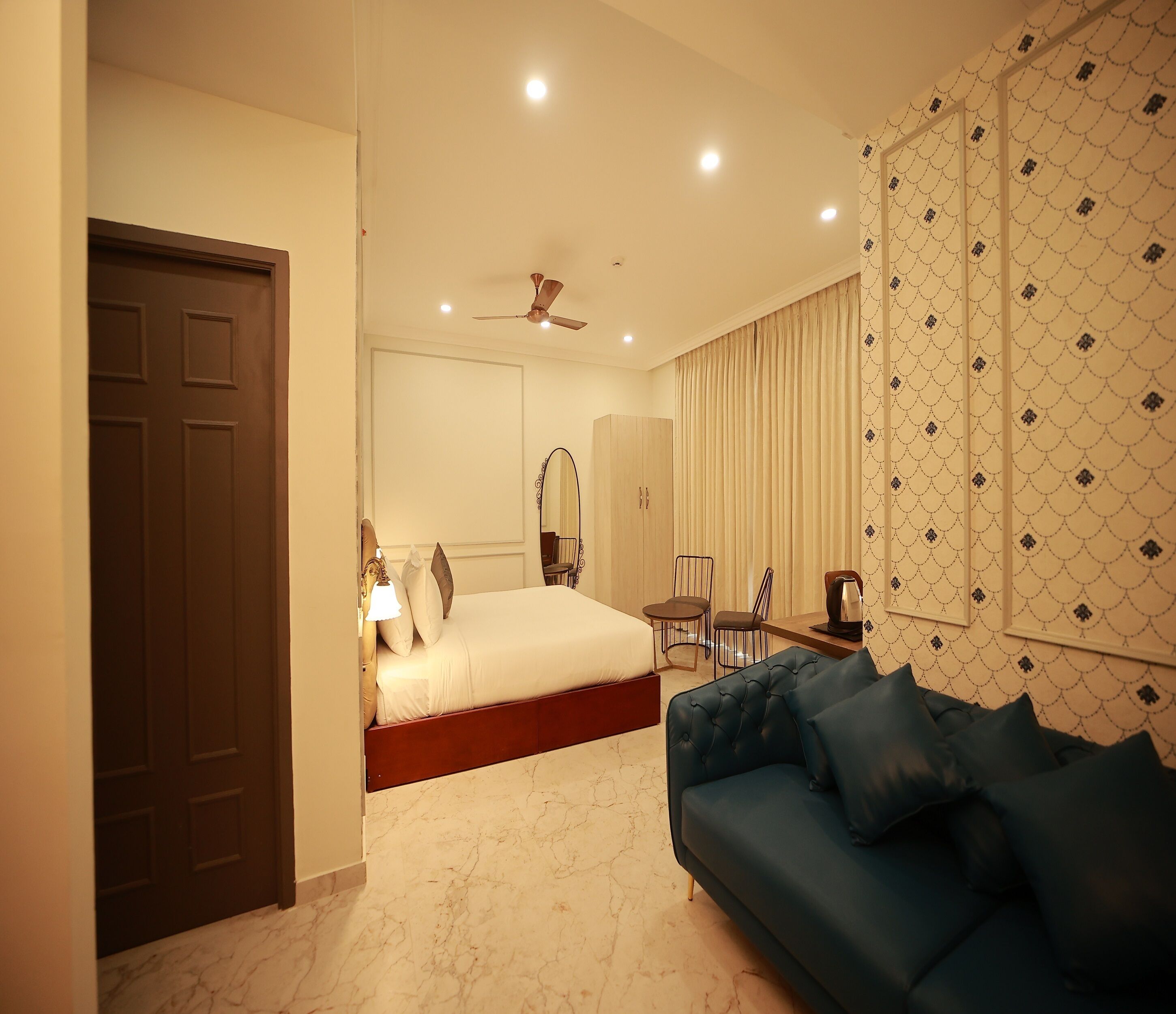 A hotel room with a bed, a blue sofa, a desk, and a mirror.