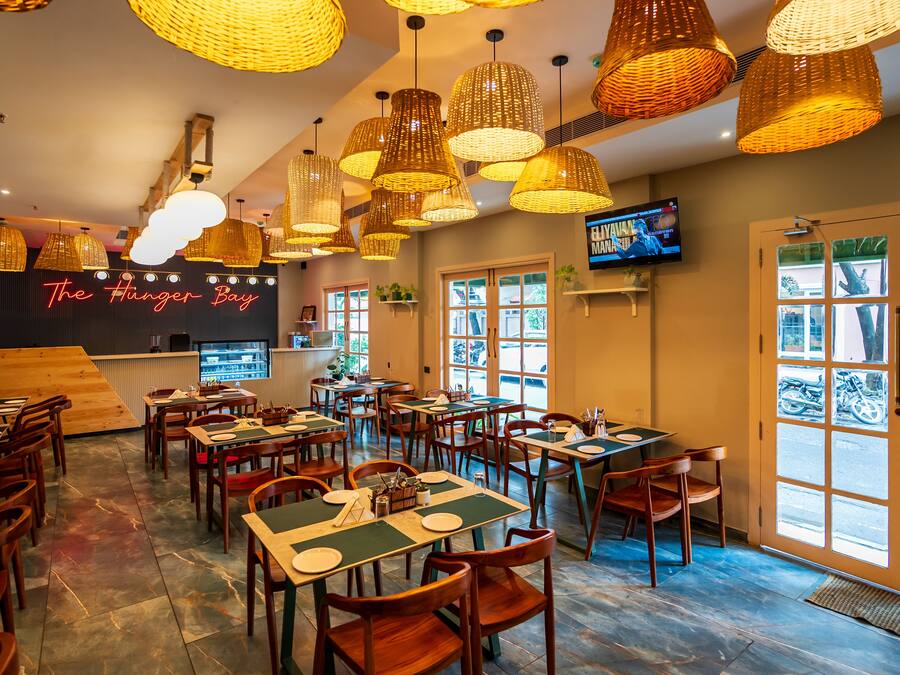A restaurant interior with multiple tables and chairs, hanging wicker lamps, and a television on the wall.