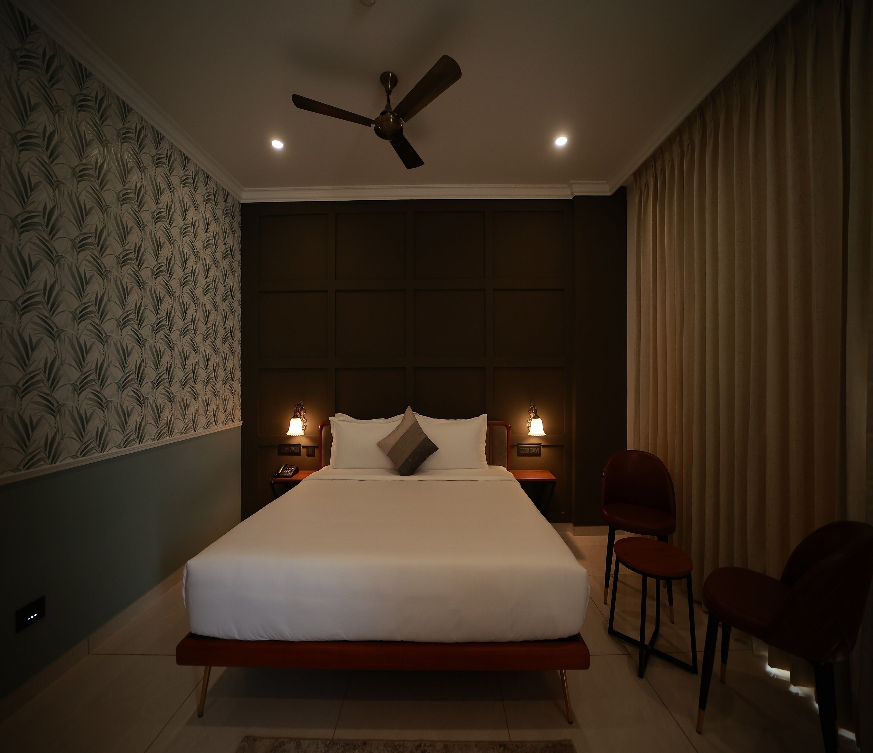 A modern bedroom with a large bed, two bedside lamps, a ceiling fan, and a patterned wallpaper on one wall.
