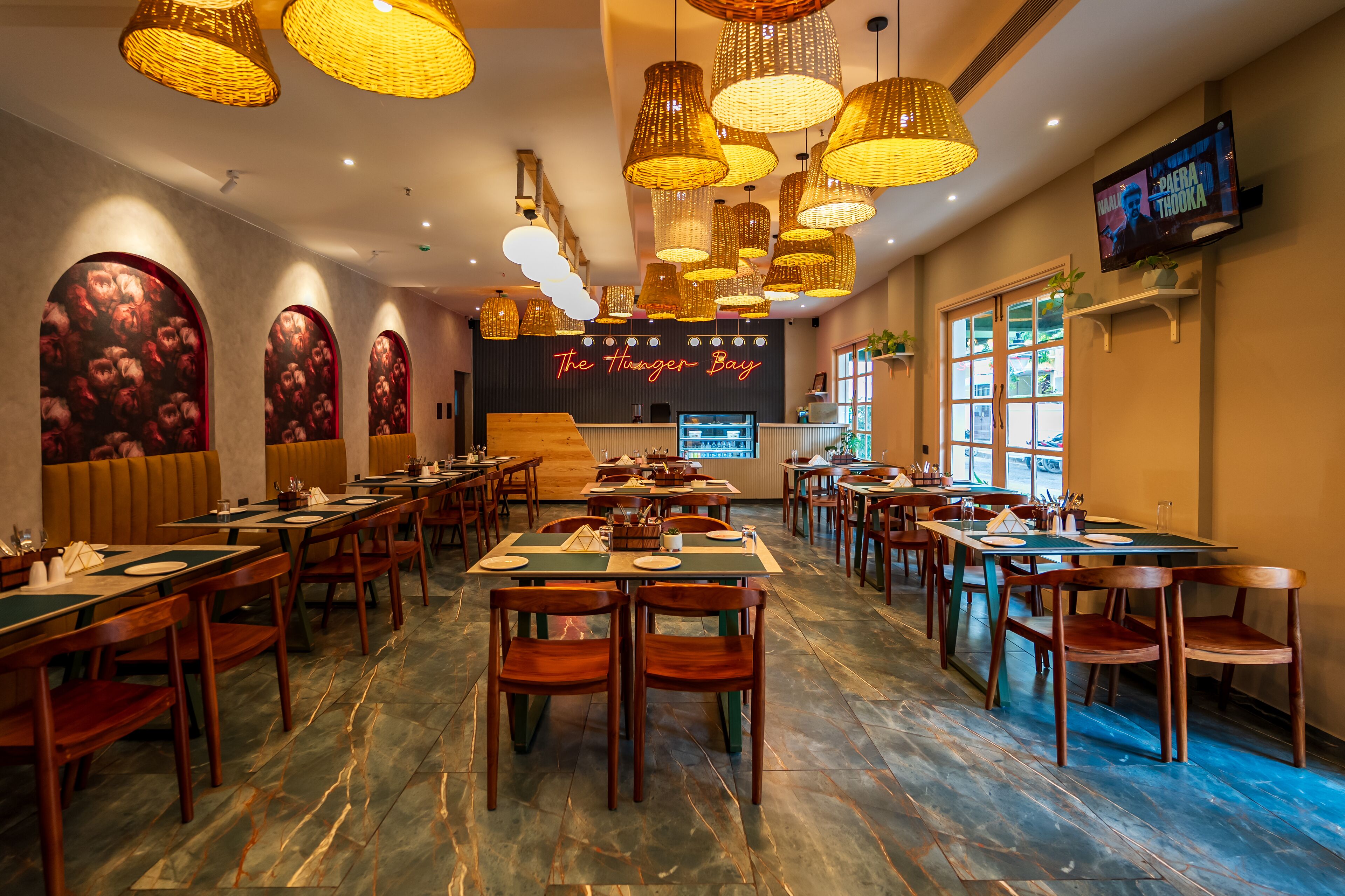 A restaurant interior with multiple tables and chairs, warm lighting, and a TV screen displaying a movie.