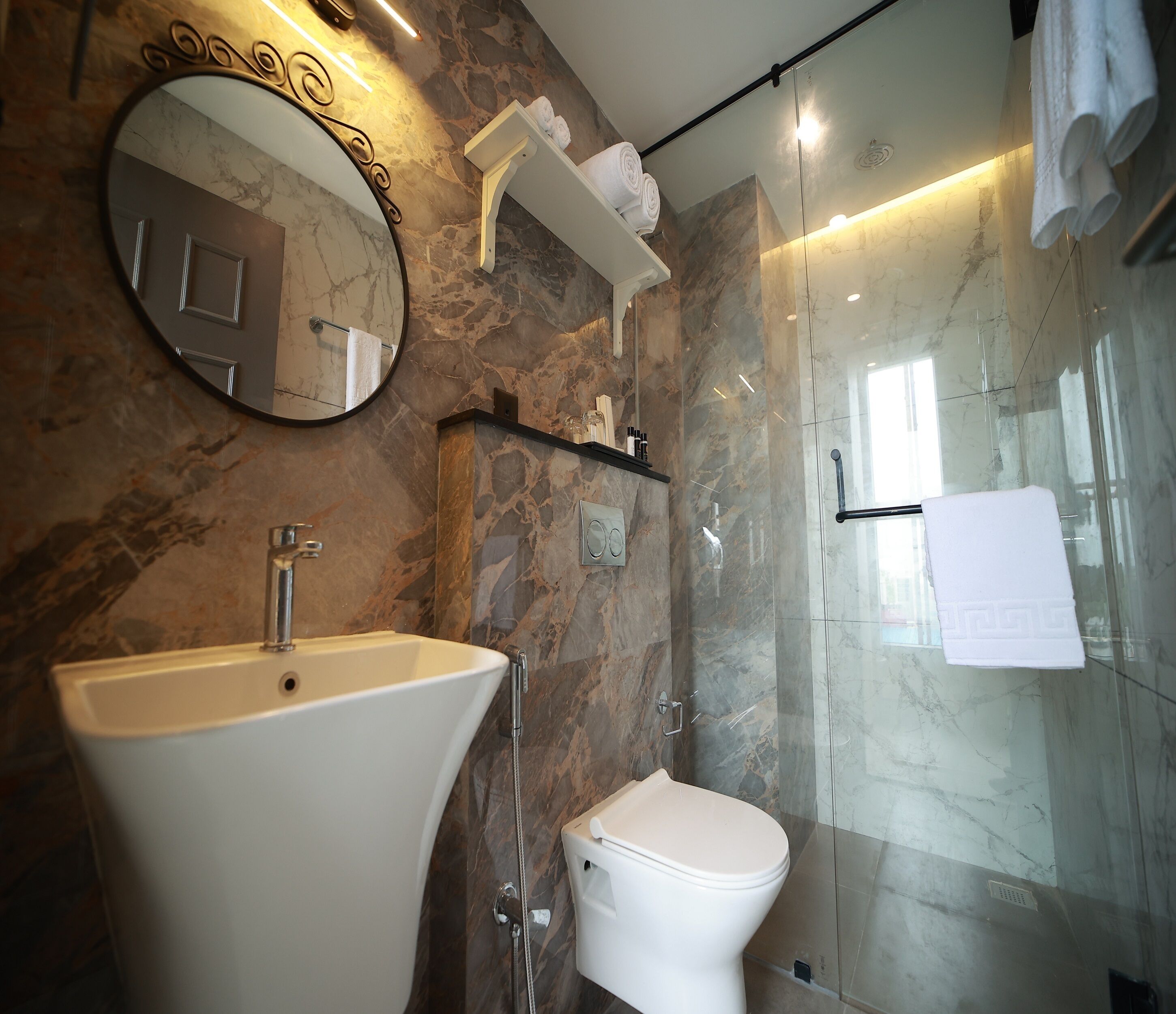 A bathroom with a marble wall, a sink, a toilet, and a glass shower enclosure.