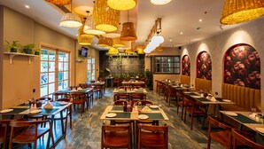 A restaurant with multiple dining tables and chairs, warm lighting, and decorative wall art. - De Fleur Hotel (Puducherry)