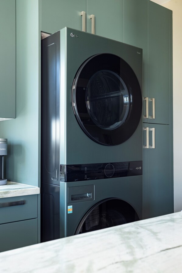 Une buanderie moderne et compacte, dotée d’un lave-linge et d’un sèche-linge à chargement frontal, de placards intégrés et d’un plan de travail en marbre.
