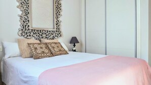 A neatly made bed with patterned pillows, a decorative wall hanging, and a bedside lamp.