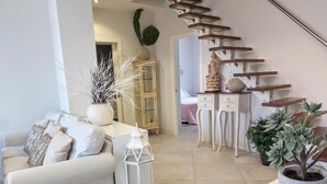 A modern living room with a white sofa, a coffee table, and decorative plants. A staircase with wooden steps leads to another room.