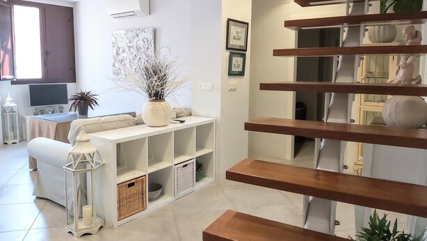 A modern living room with a sofa, a coffee table, a TV, and a staircase with wooden steps.
