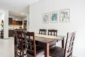 Ein Essbereich mit Holztisch und -stühlen, im Hintergrund eine Küche und drei gerahmte Kunstwerke an der Wand.