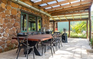 A covered outdoor dining area with a stone wall, wooden pergola, and a table with chairs. - Casa Rua | Margaret River (Witchcliffe)
