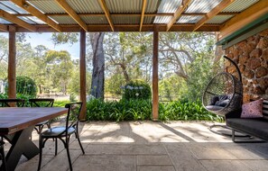 An outdoor patio with a wooden table and chairs, a hanging chair, and a stone wall. - Casa Rua | Margaret River (Witchcliffe)