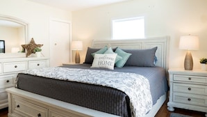 A bedroom with a bed, bedside tables, a dresser, a mirror, and a window.