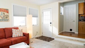 A living room with a sofa, a rug, a door, and a view into a kitchen.