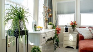 Una habitación bien iluminada con un escritorio blanco, un sofá rojo y varias plantas.