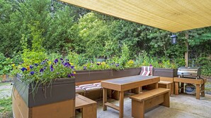 Une terrasse extérieure avec des meubles en bois, un barbecue et un espace ombragé agrémenté de guirlandes lumineuses.