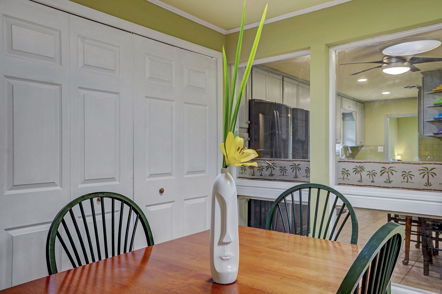 A dining area with a wooden table, two chairs, and a vase with yellow flowers.