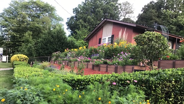 Une maison à l’extérieur en briques, entourée d’un jardin bien entretenu où poussent différentes plantes à fleurs et où une haie est taillée avec soin.