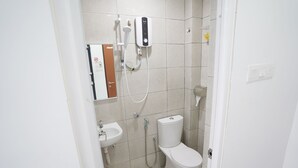 Une petite salle de bain propre, équipée de toilettes, d’un lavabo et d’une douchette fixée au mur.