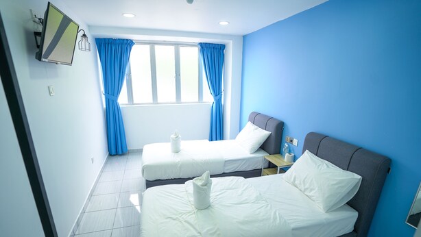 Une chambre d’hôtel avec deux lits, un téléviseur à écran plat, une fenêtre avec des rideaux bleus et une salle de bain visible dans un coin.