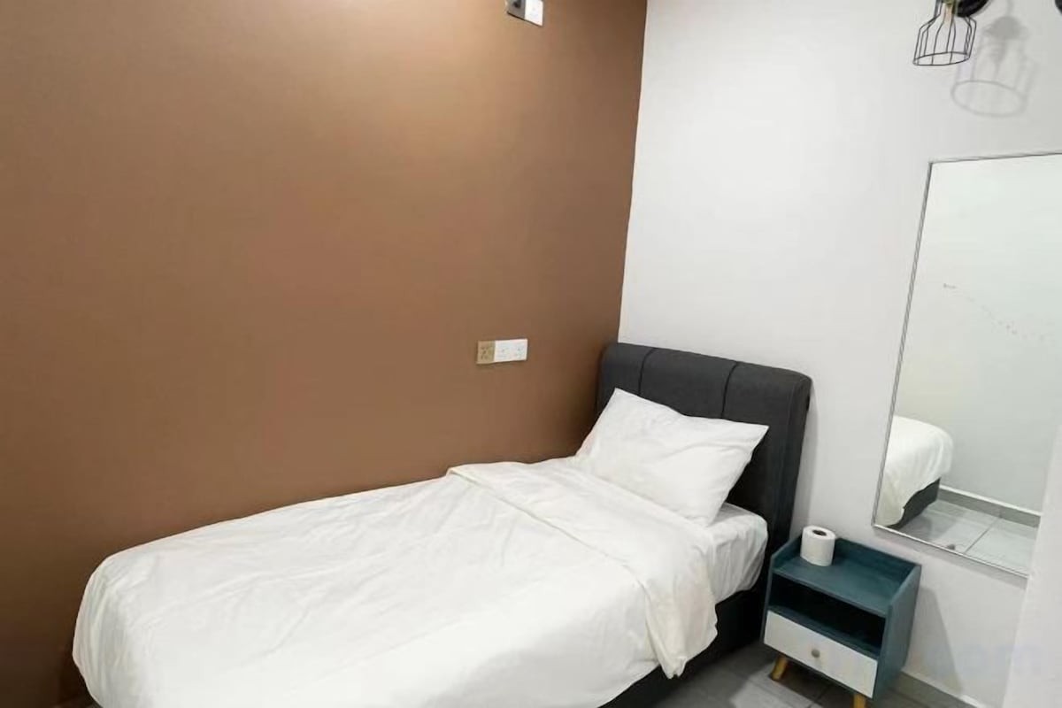 A single bed with white bedding in a room with brown walls, a small bedside table with a white tissue box, and a mirror on the wall.
