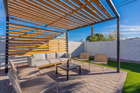 An outdoor patio with a wooden pergola, a sofa, two wicker chairs, and a table. - Old Town Retreat • Luxe Pool & Outdoor Space for Relaxing Getaways (Scottsdale)