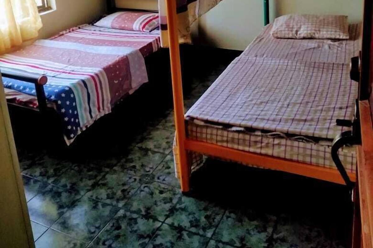 A dormitory room with two bunk beds, a window with curtains, and a tiled floor.