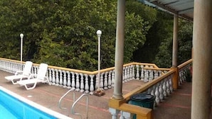 Un espacio al aire libre techado con piscina, sillas de descanso y mesas.