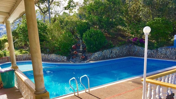 Una piscina con pared de piedra y vegetación al fondo.