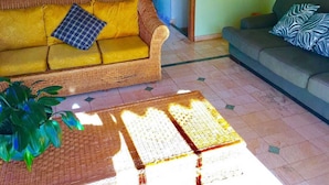 Una sala de estar con un sofá amarillo, un sofá gris y una mesa de centro trenzada.