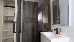 A modern bathroom with a walk-in shower, a large mirror, and a white sink with toiletries. - NEWLY Renovated 2bed/1bath home! (Los Angeles)