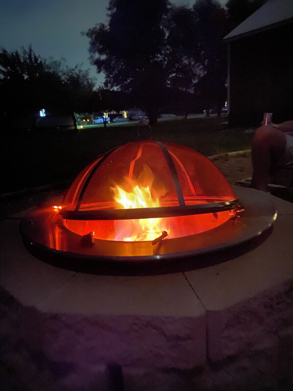 A fire pit with a metal grill and a fire burning inside, surrounded by a concrete base.