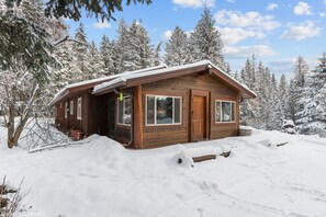 Eine Holzhütte mit geneigtem Dach, großen Fenstern und einer Tür.