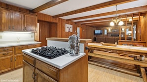 A wooden cabin interior with a kitchen area featuring a stove, wooden cabinets, and a dining table with benches. - The Lazy Bear - Mountain Retreat with Sauna (Whitefish)