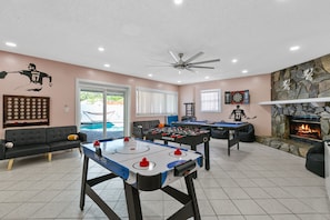 A room with a foosball table, a pool table, a fireplace, and a ceiling fan.