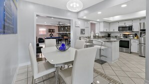 A modern kitchen with white cabinetry, stainless steel appliances, and a central island with bar stools. - Tampa's Paradise (Tampa)