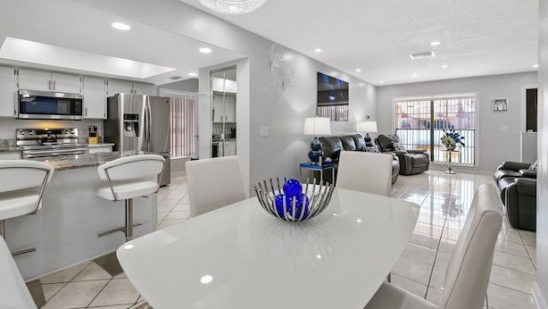 A modern kitchen with stainless steel appliances, a dining area with a white table, and a living room with leather sofas. - Tampa's Paradise (Tampa)